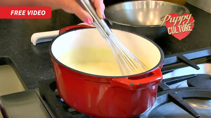 A hand whisking pudding in a red enamel pot on a stove